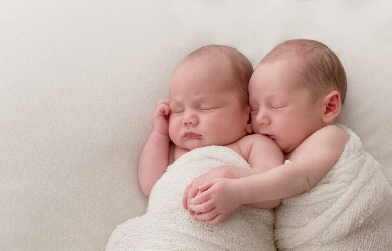 Newborn brother holds twin sister's hand and kisses her shoulder