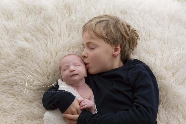 Big brother hugging and kissing newborn sister