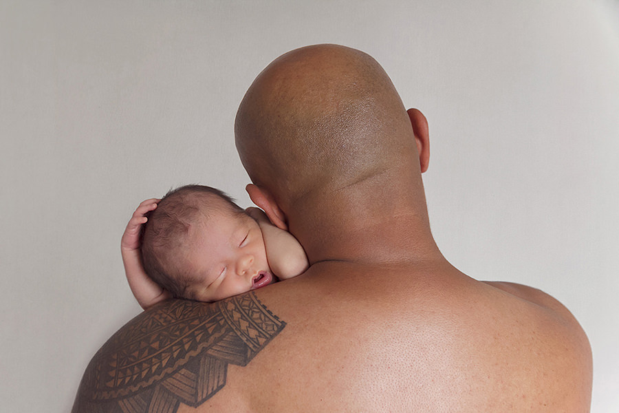 Father with large tattoo comforts baby son on his shoulder