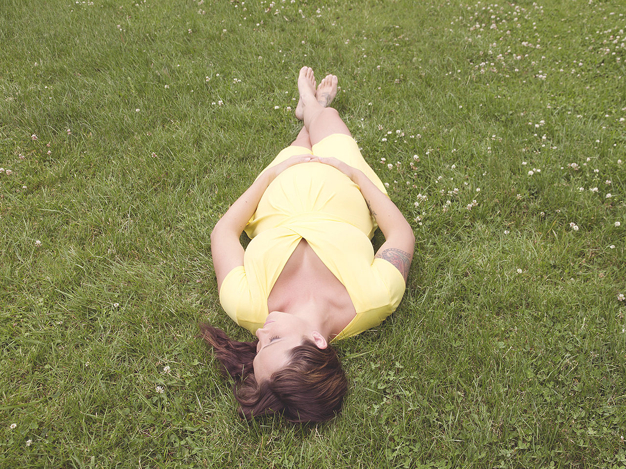 Pregnant lady lying on grass in yellow dress