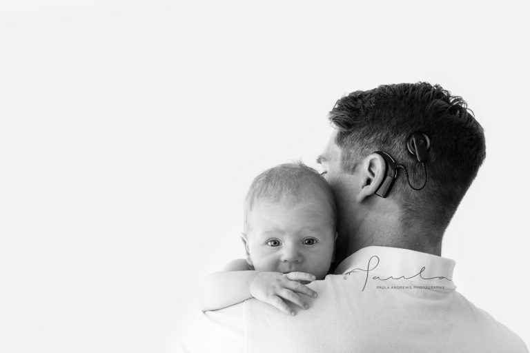 Father with hearing aid hugging newborn son