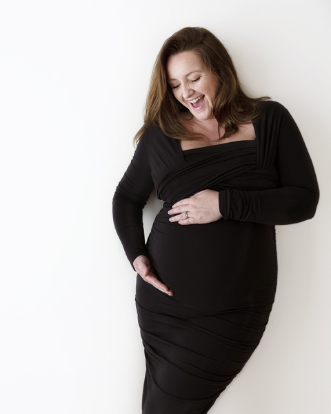 plus sized pregnant lady in figure hugging black dress laughing