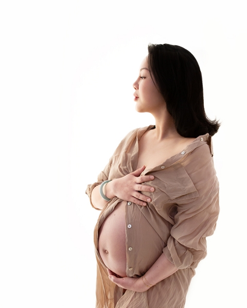 pregnant lady in oversized beige shirt at maternity photoshoot at Paula Andrews Photography
