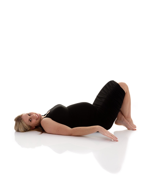 Pregnant blonde mother-to-be lying on reflective floor in black dress