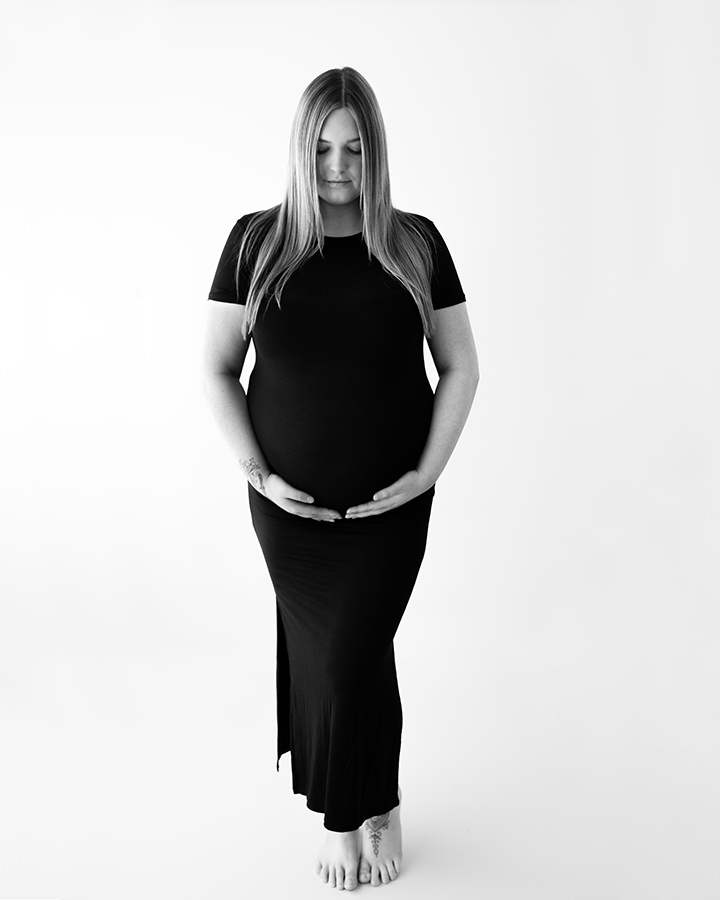 Blonde haired pregnant woman in black dress at maternity photoshoot