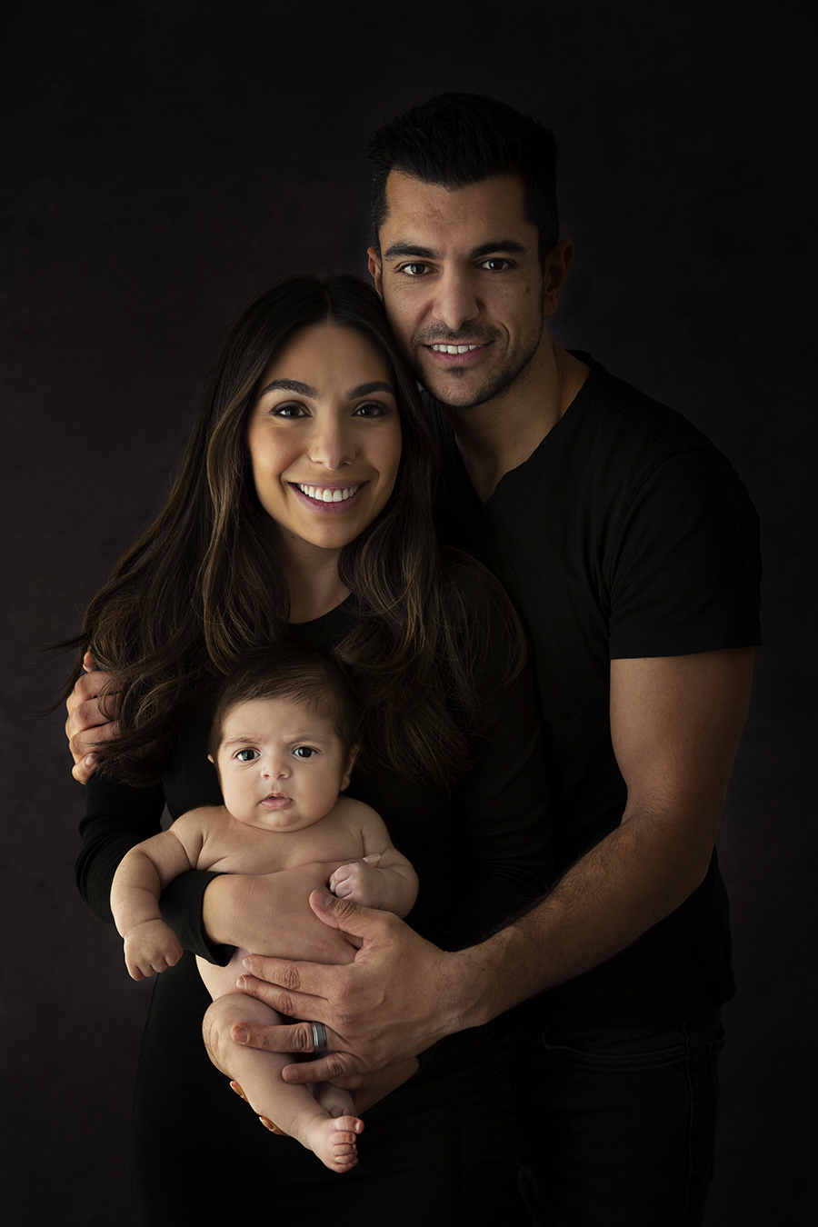 Dark moody portrait of new parents cuddling their newborn baby